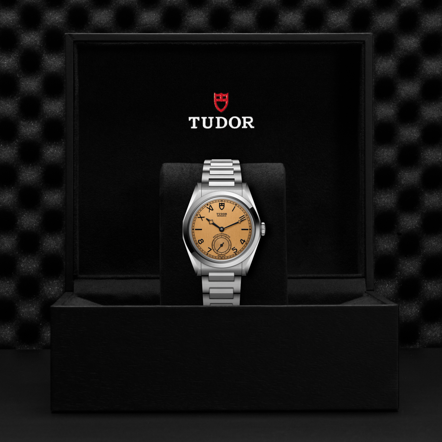 Tudor Monarch watch with steel bracelet and champagne dial in a black box against a black background.