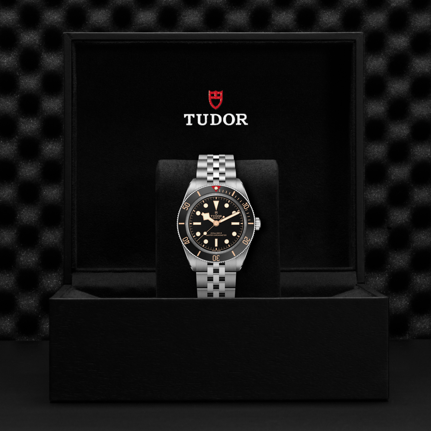 Tudor Black Bay 58 watch with a steel bracelet and black dial in a black box against a black background.