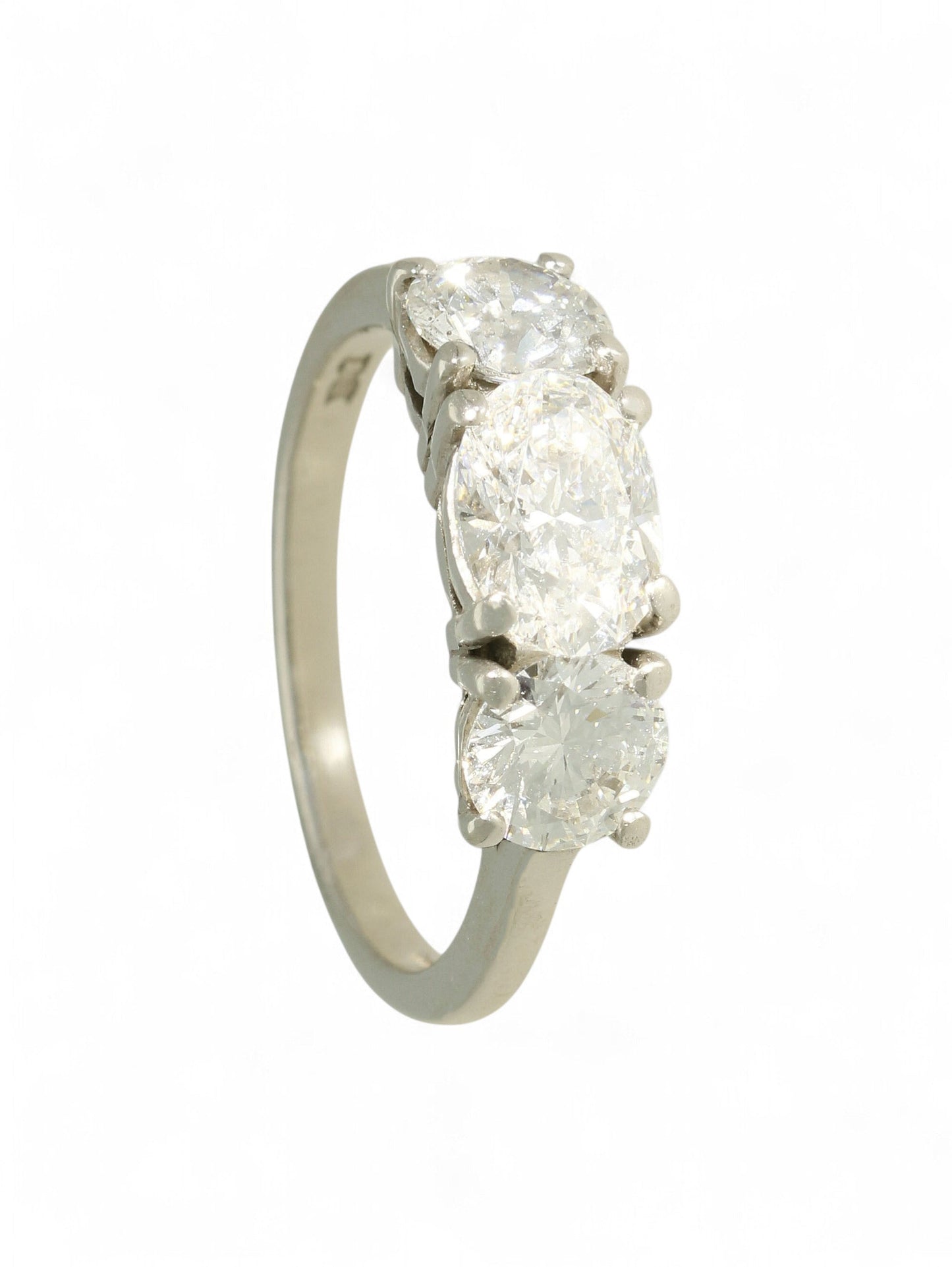Platinum three-stone diamond ring with oval-cut centre and two round brilliant-cut stones on a white background.