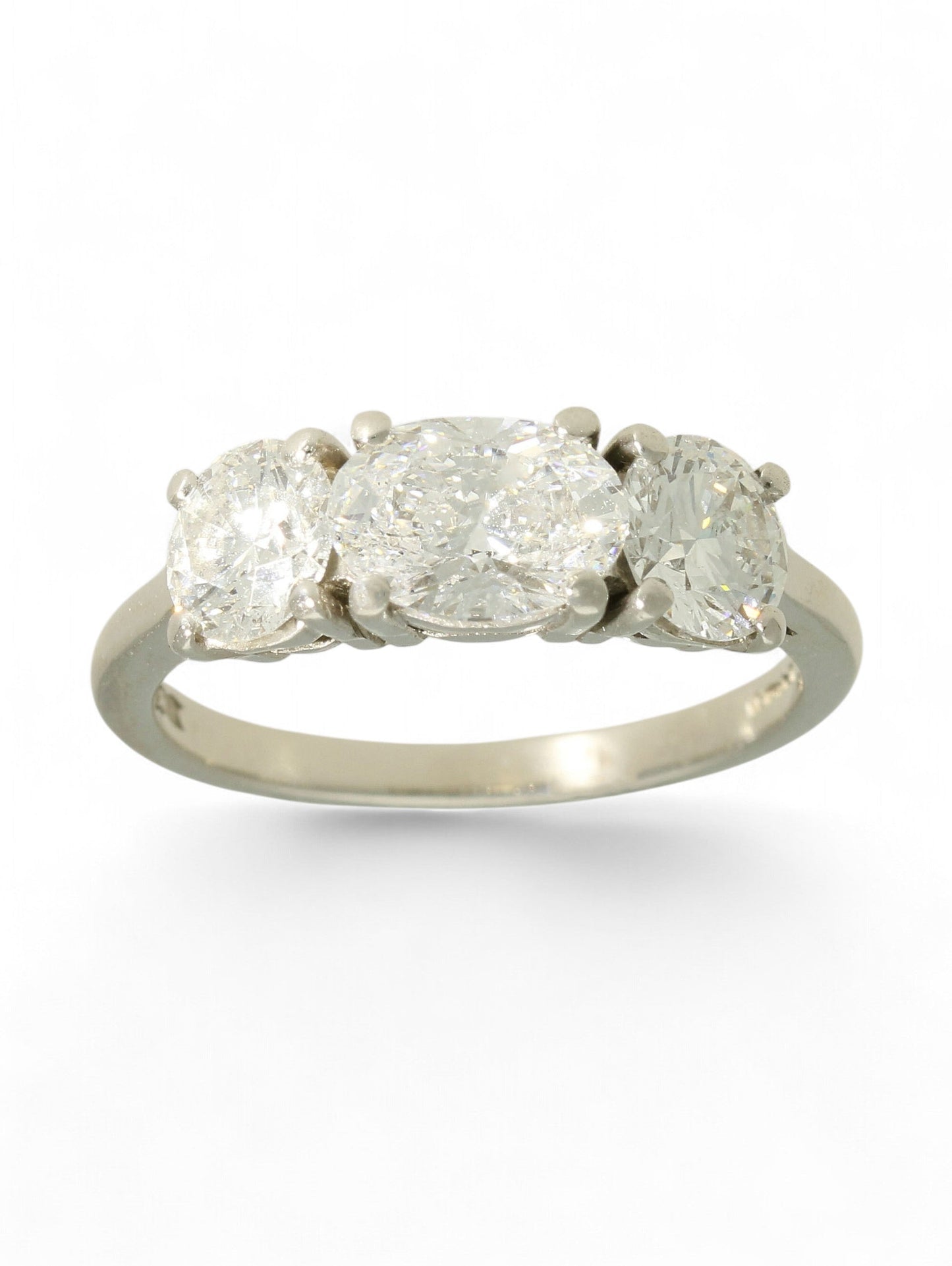 Platinum three-stone diamond ring with oval-cut centre and two round brilliant-cut stones on a white background.