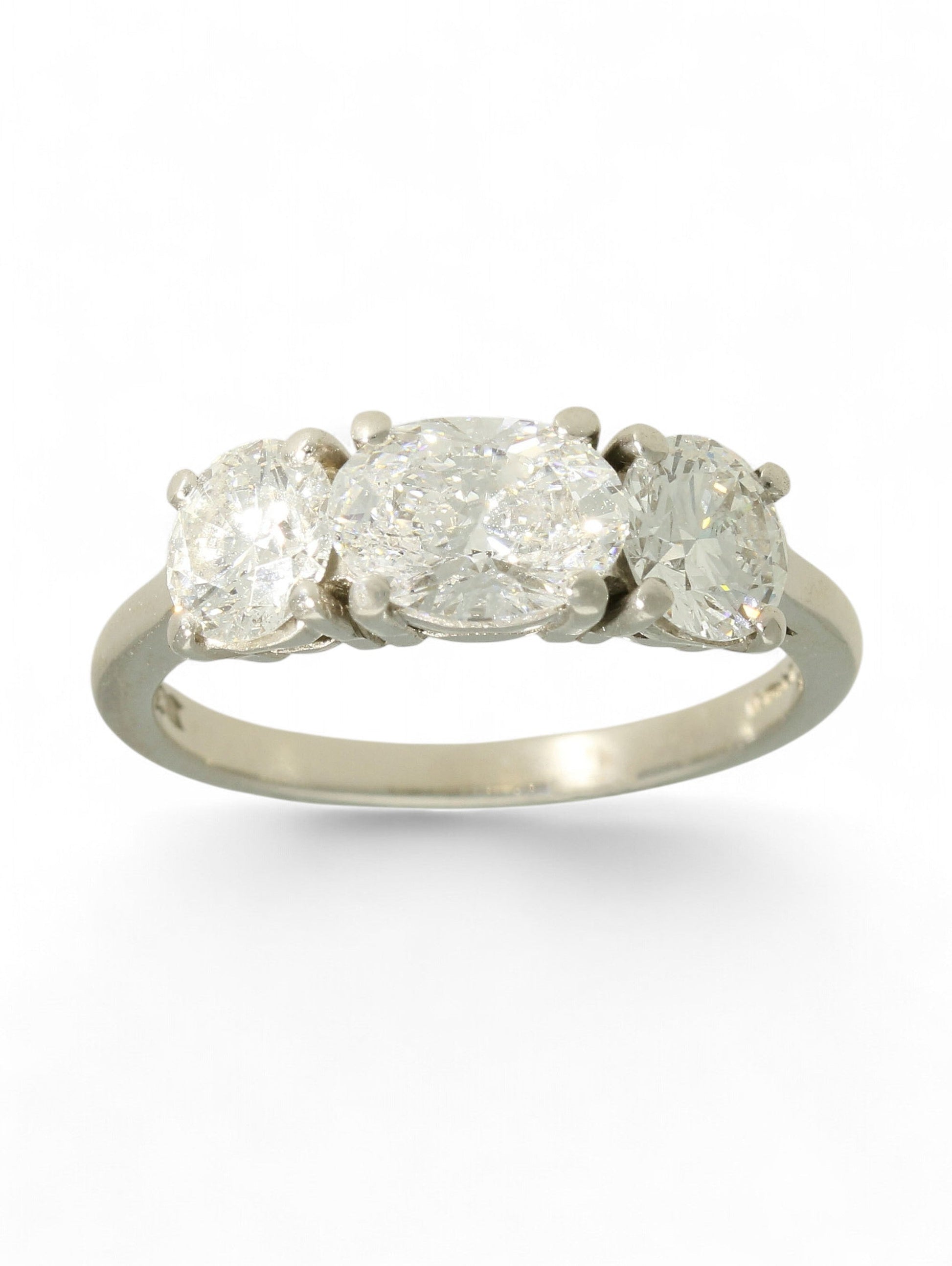 Platinum three-stone diamond ring with oval-cut centre and two round brilliant-cut stones on a white background.