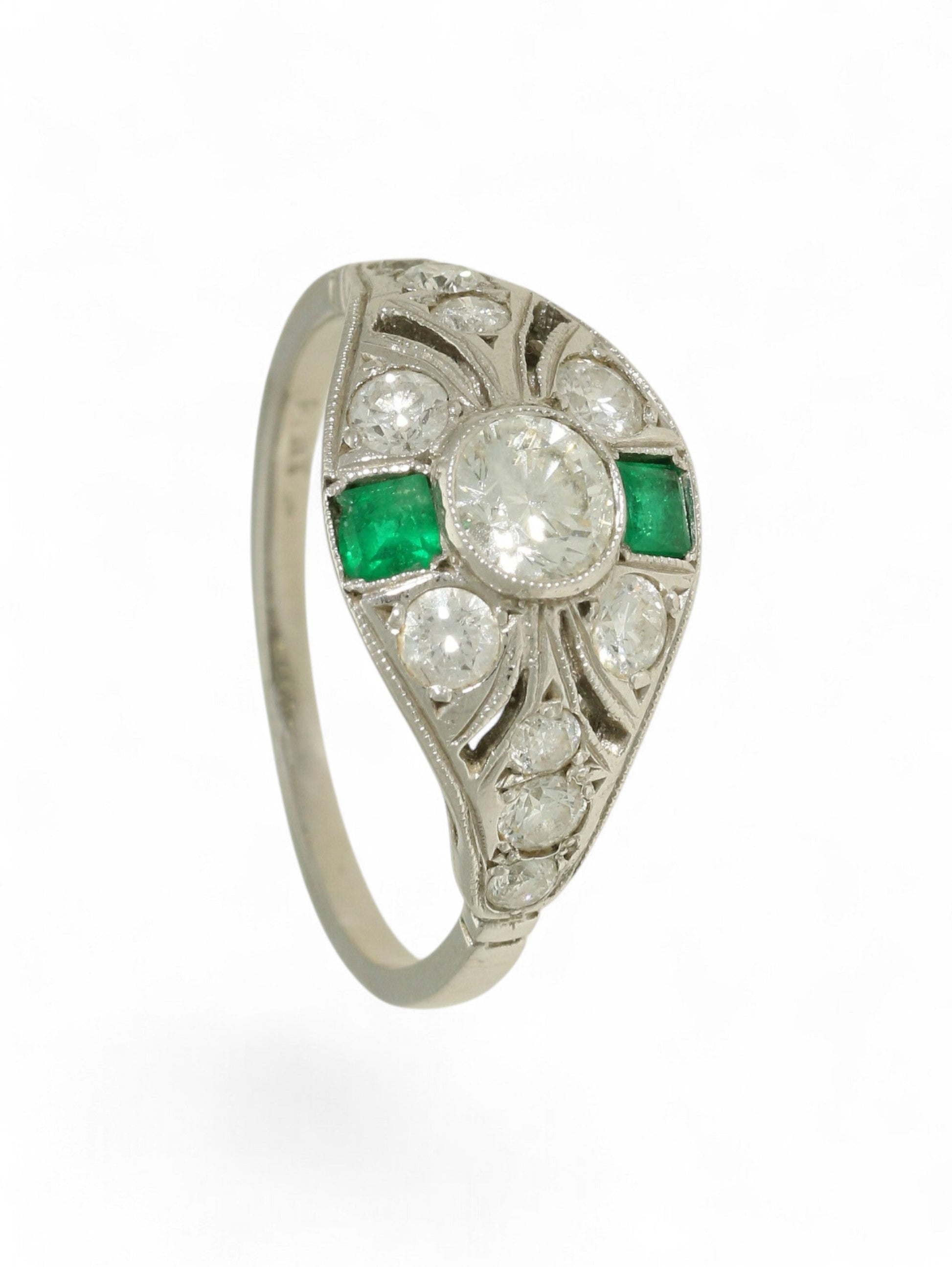 Platinum art deco-style ring with round-cut diamonds and square-cut emeralds on a white background.
