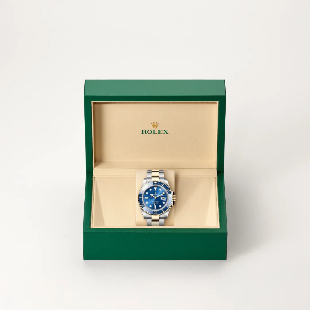 Rolex Submariner Date watch in a green and beige presentation box on a light background.