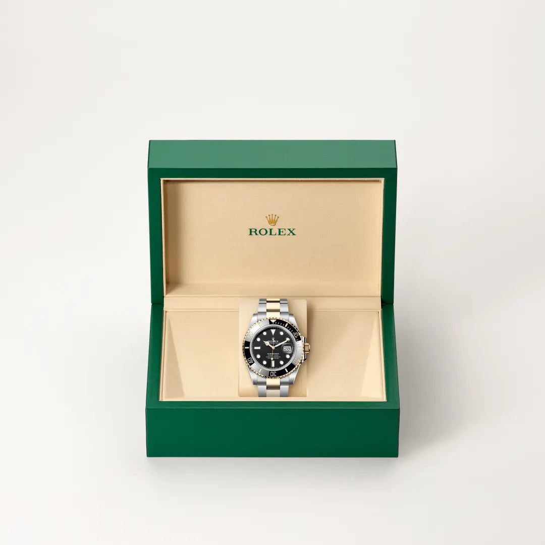 Rolex Submariner Date watch in a green and beige presentation box on a light background.