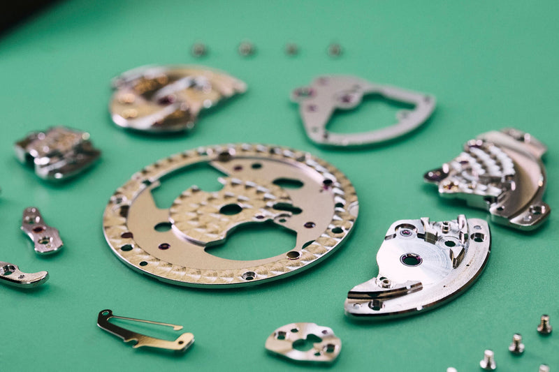 Close-up of watch movement components arranged on a green background.
