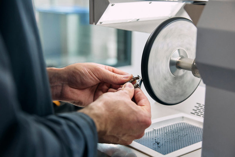 Watchmaker polishing a watch case using a polishing wheel.
