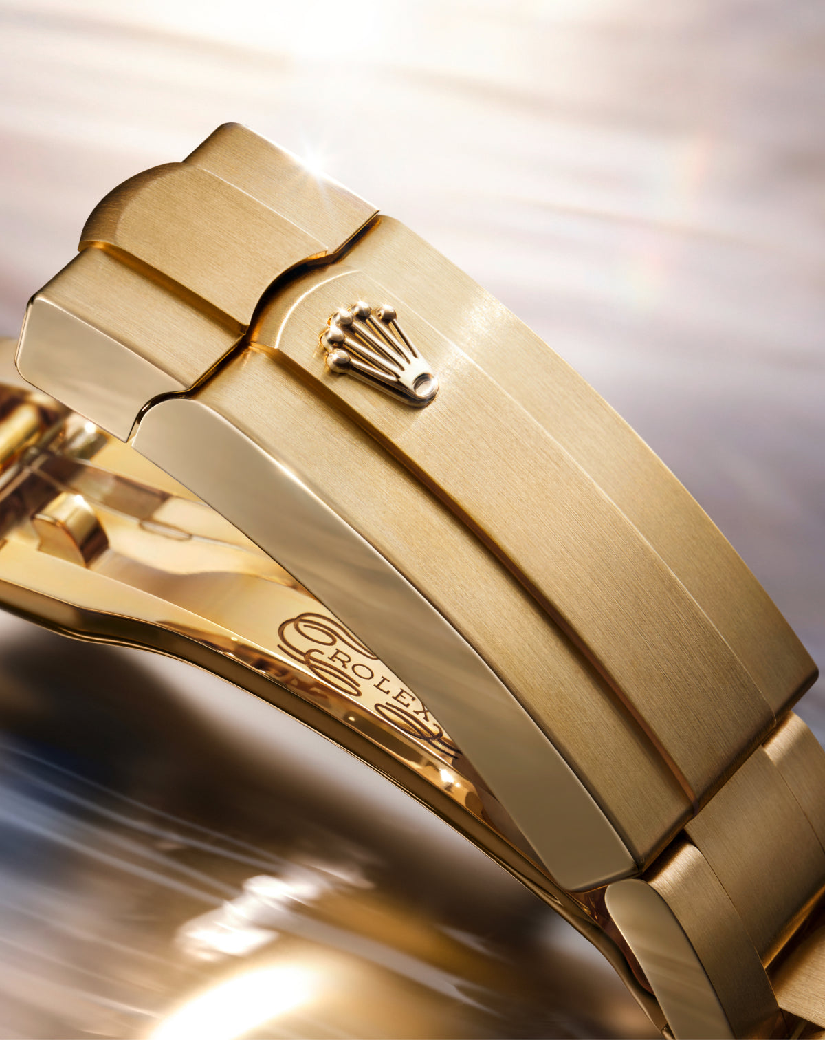 Close-up of yellow gold Rolex clasp on a reflective background.