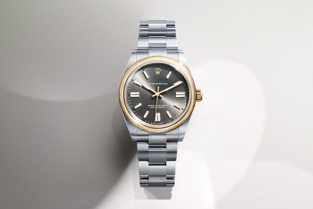 Rolex Oyster Perpetual watch with a steel bracelet, yellow-gold bezel and slate dial on a reflective background.