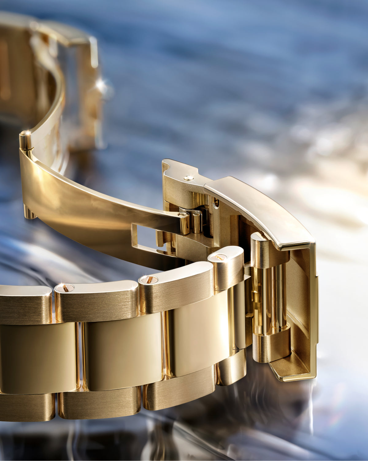 Yellow-gold Rolex Oyster bracelet on a reflective background.