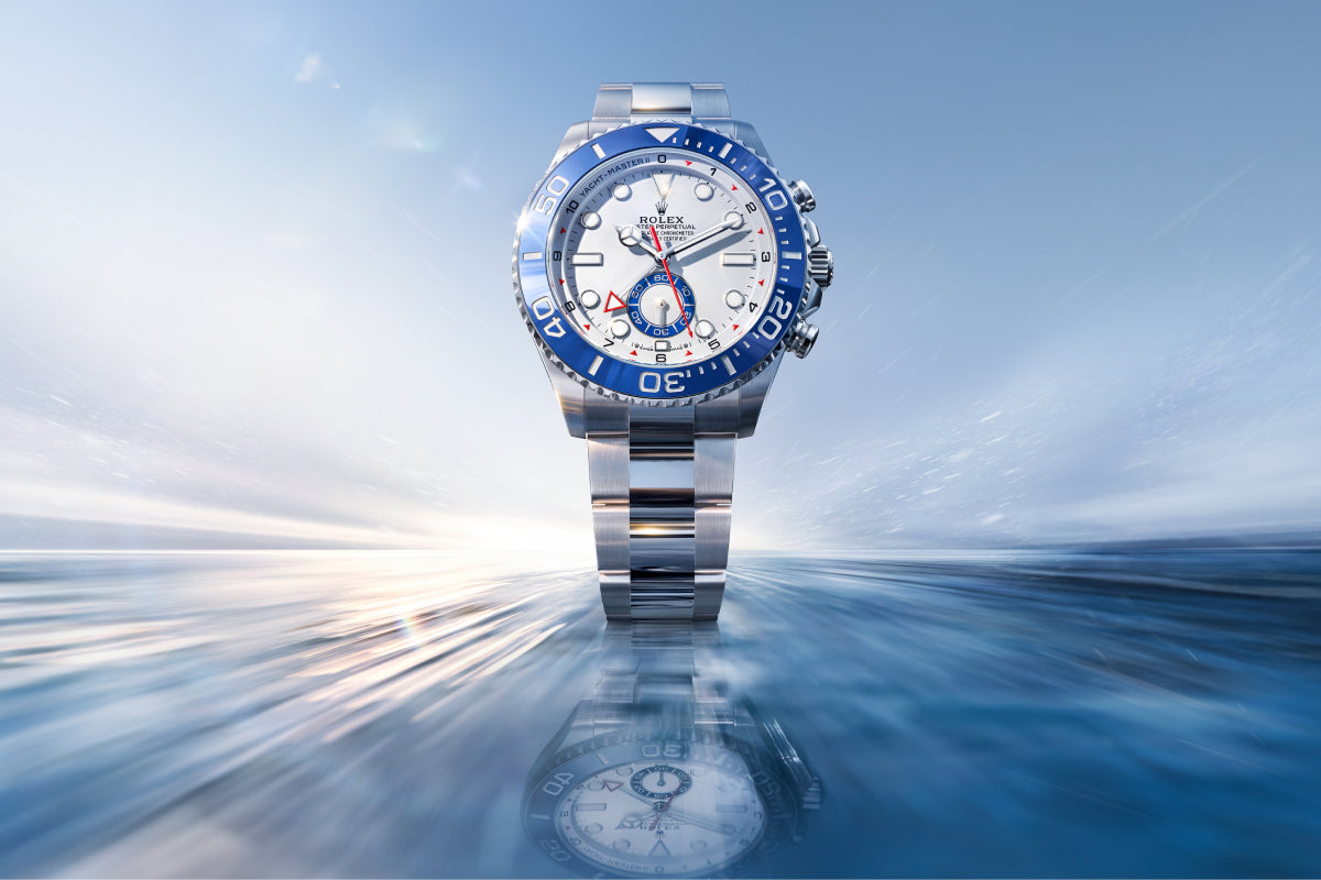 Rolex Yacht-Master II watch with a blue bezel, steel bracelet, and white dial on a reflective background.