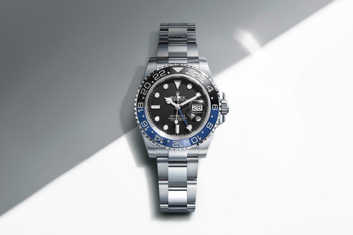 Rolex GMT-Master II watch with a steel bracelet, blue and black bezel, and black dial on a reflective background.