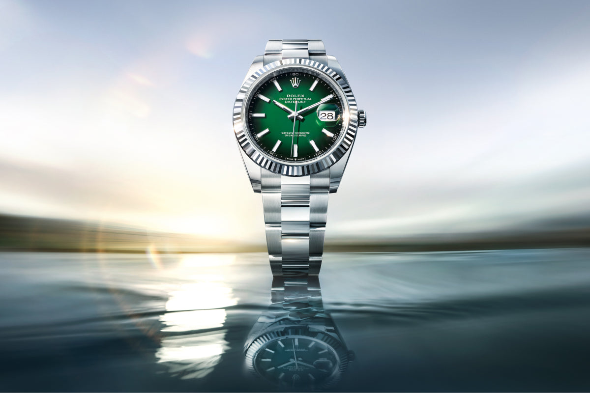 Rolex Datejust 41 watch with a fluted bezel, steel bracelet, and green dial on a reflective background.