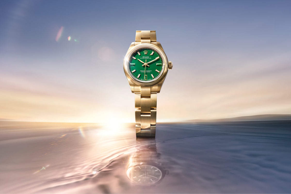 Rolex Oyster Perpetual 28 watch with a yellow gold bracelet and green dial on a reflective background.