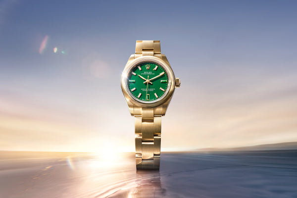 Rolex Oyster Perpetual 28 watch with a gold bracelet and green dial on a sea and sky background.