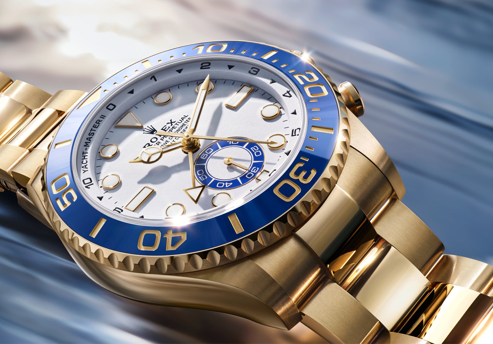 Rolex Yacht-Master II with a yellow-gold bracelet, blue bezel and white dial on a reflective background.