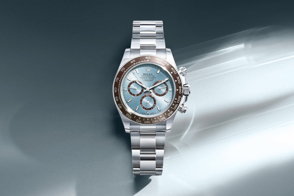 Rolex Cosmograph Daytona watch with a platinum bracelet and blue dial on a reflective background.