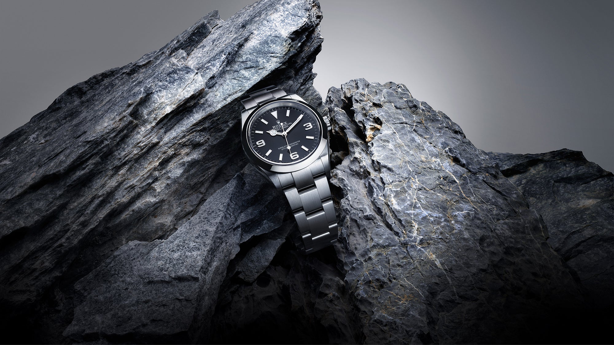 Rolex Explorer watch with a steel bracelet and black dial on a rocky background.