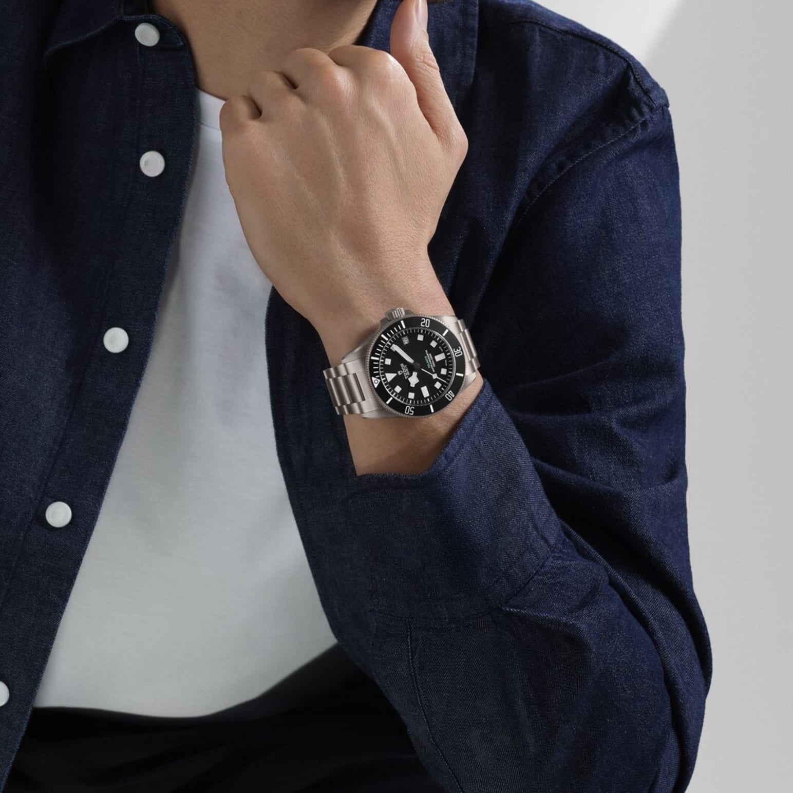 Person wearing a Tudor Pelagos Ultra watch with a black dial and steel bracelet, dressed in a navy blue shirt.