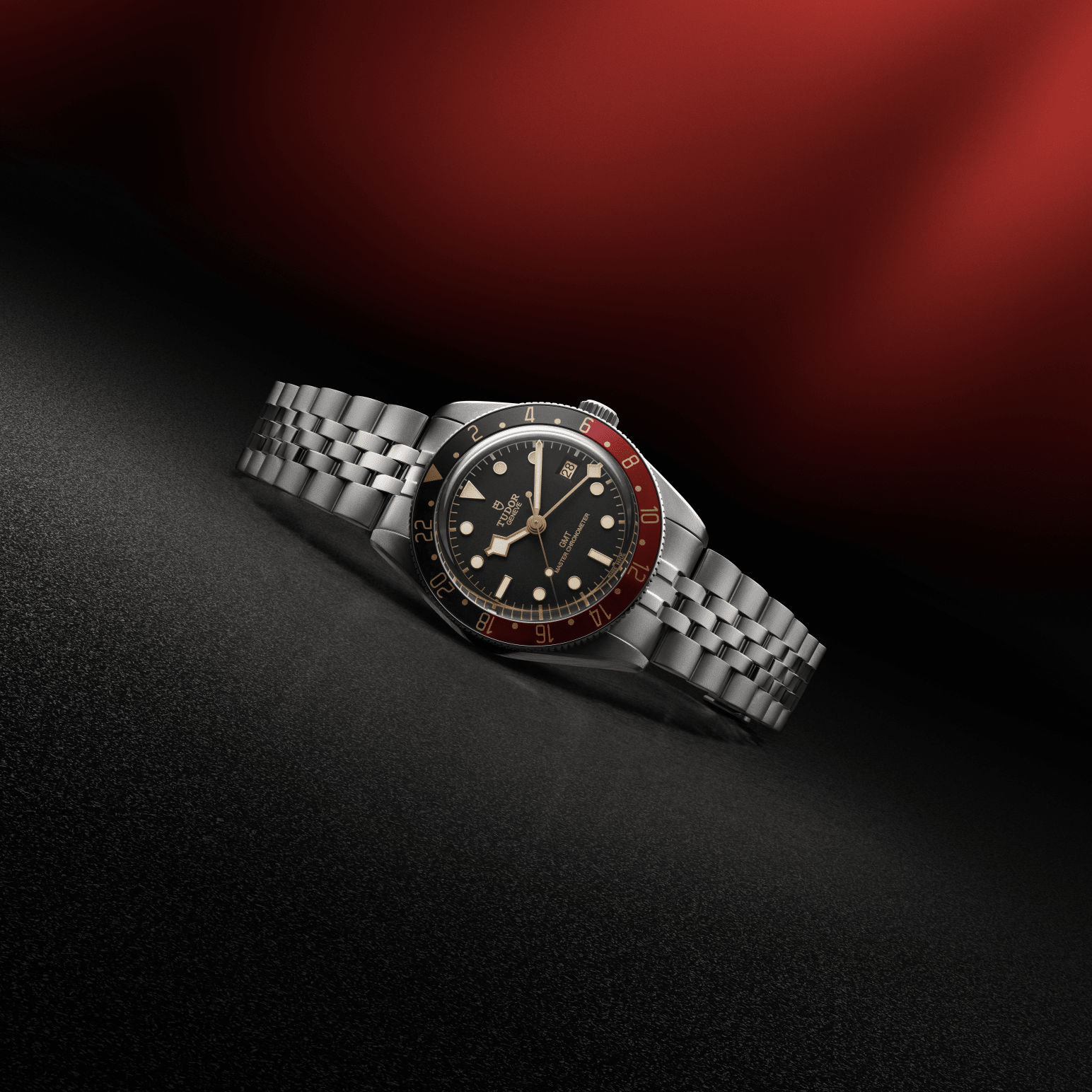Tudor Black Bay 58 GMT watch with a steel bracelet and black dial lying sideways on a black and red background.