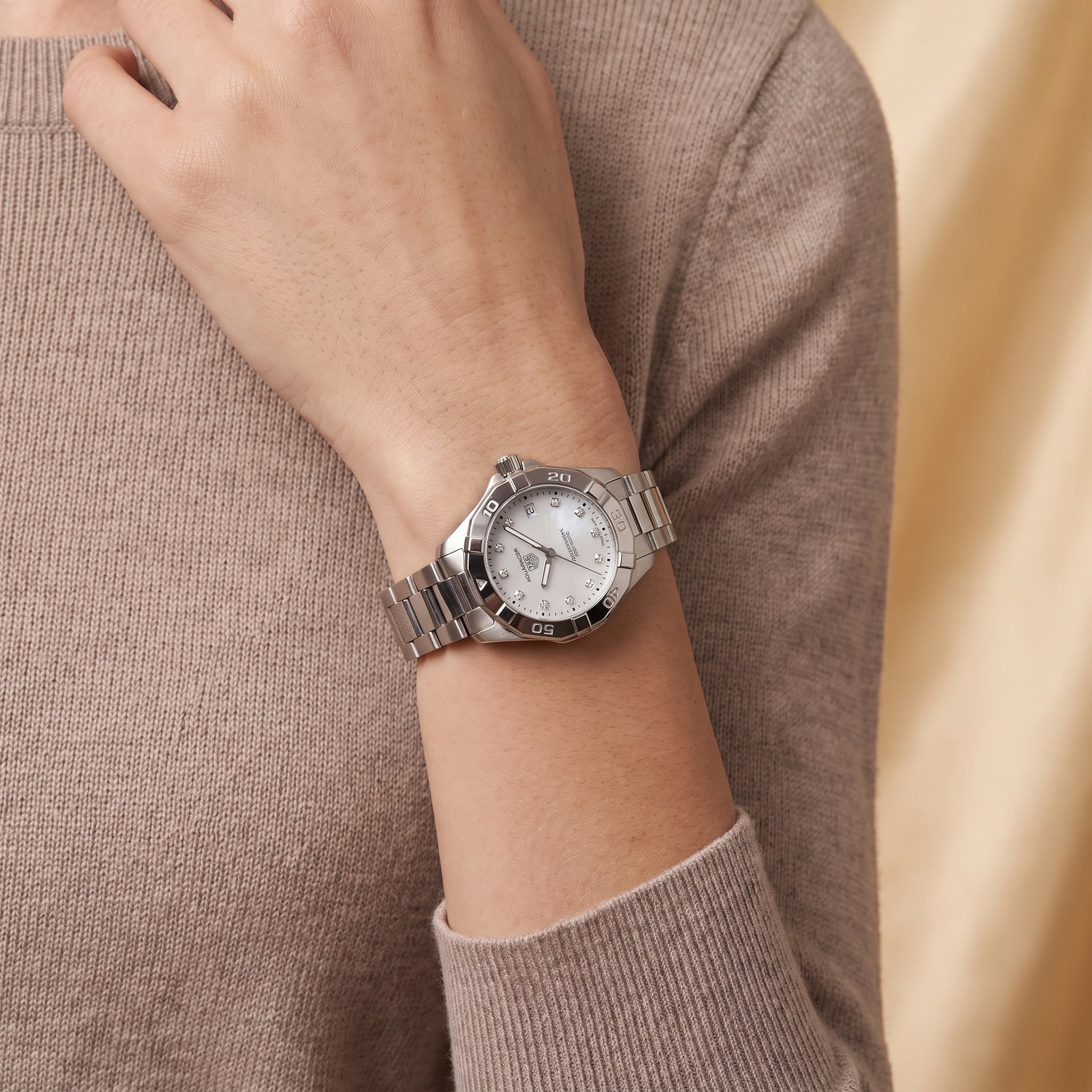 TAG Heuer Aquaracer with 34mm case, steel bracelet and white mother of pearl, diamond-set dial on a women's wrist.