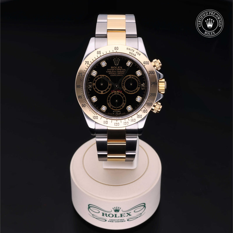 Rolex Cosmograph Daytona with Oystersteel and 18ct yellow gold case, Oyster bracelet & black dial, on a cream presentation stand against a black background.Cosmograph Daytona