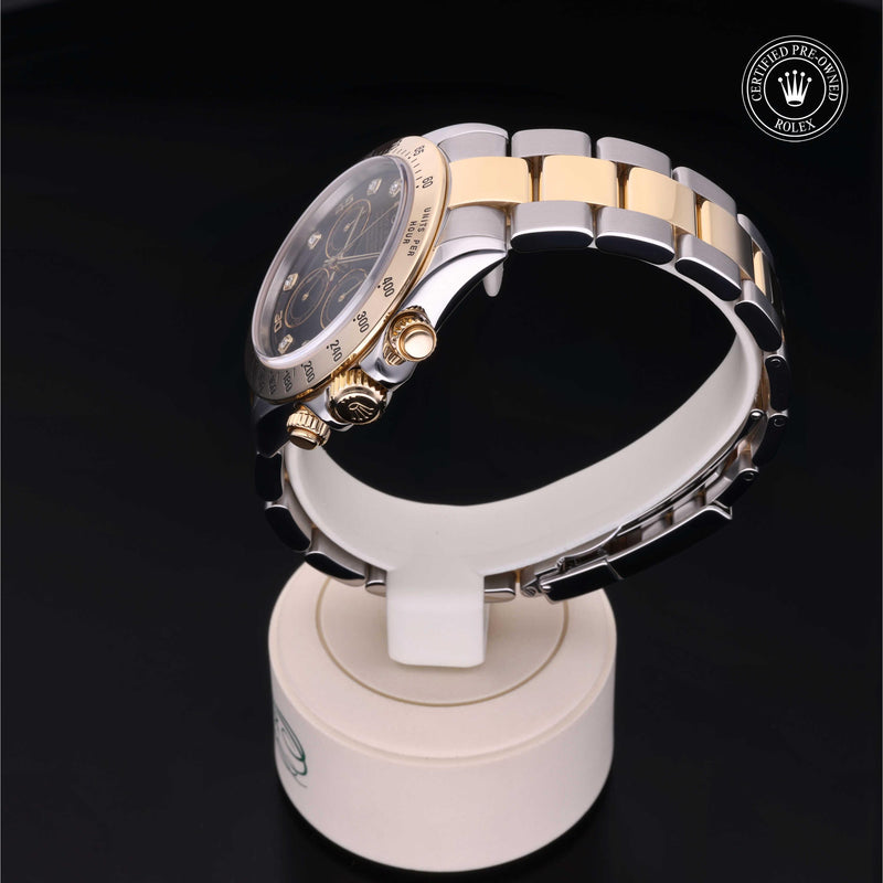 Rolex Cosmograph Daytona with Oystersteel and 18ct yellow gold case, Oyster bracelet & black dial, on a cream presentation stand against a black background.Cosmograph Daytona