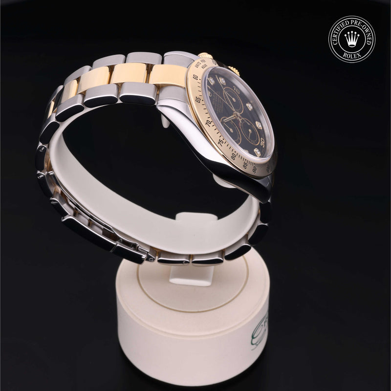 Rolex Cosmograph Daytona with Oystersteel and 18ct yellow gold case, Oyster bracelet & black dial, on a cream presentation stand against a black background.Cosmograph Daytona