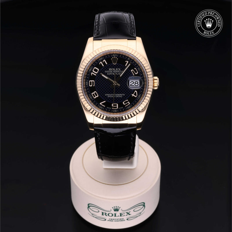 Rolex Datejust 36 with 18ct yellow gold case, black leather strap & black dial, on a cream presentation stand against a black background.Datejust 36