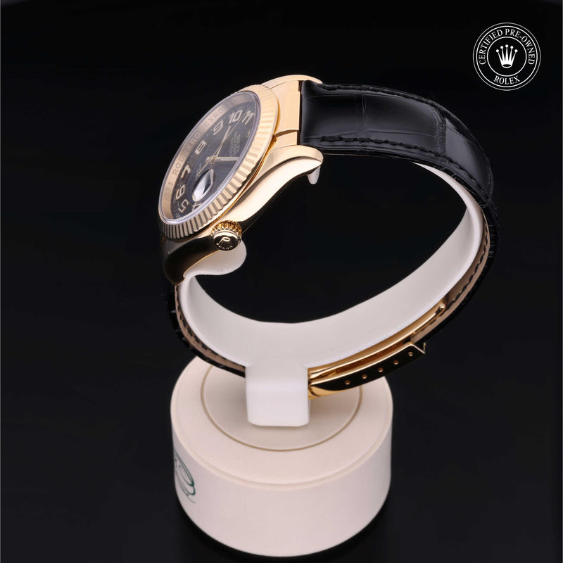 Rolex Datejust 36 with 18ct yellow gold case, black leather strap & black dial, on a cream presentation stand against a black background.Datejust 36
