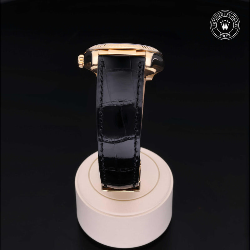 Rolex Datejust 36 with 18ct yellow gold case, black leather strap & black dial, on a cream presentation stand against a black background.Datejust 36