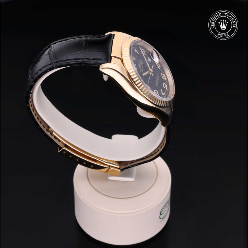 Rolex Datejust 36 with 18ct yellow gold case, black leather strap & black dial, on a cream presentation stand against a black background.Datejust 36