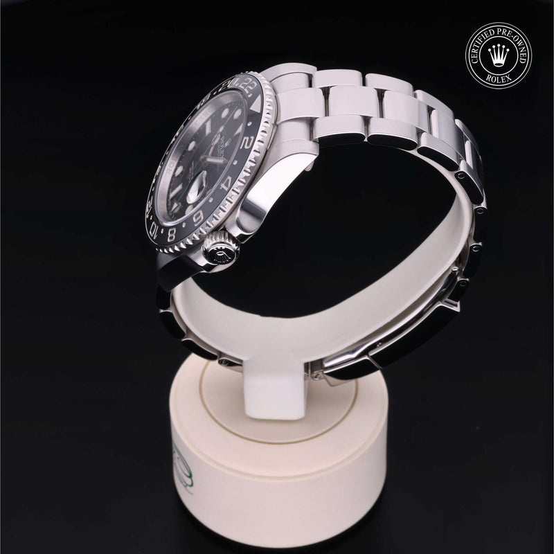 Rolex GMT-Master II with steel Oyster bracelet and black dial, on a cream presentation stand against a black background.GMT-Master II