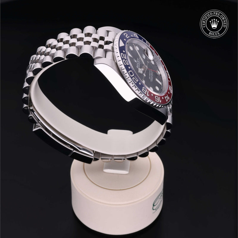 Rolex GMT-Master II with Jubilee bracelet, blue & red bezel and black dial, on a cream presentation stand against a black background.GMT-Master II