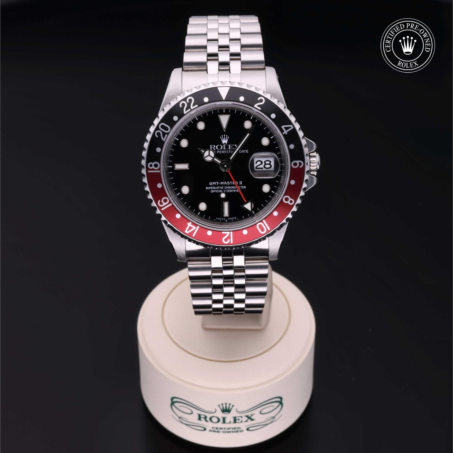 Rolex GMT-Master II with Jubilee bracelet, red and black bezel and black dial on a presentation stand against a black background.