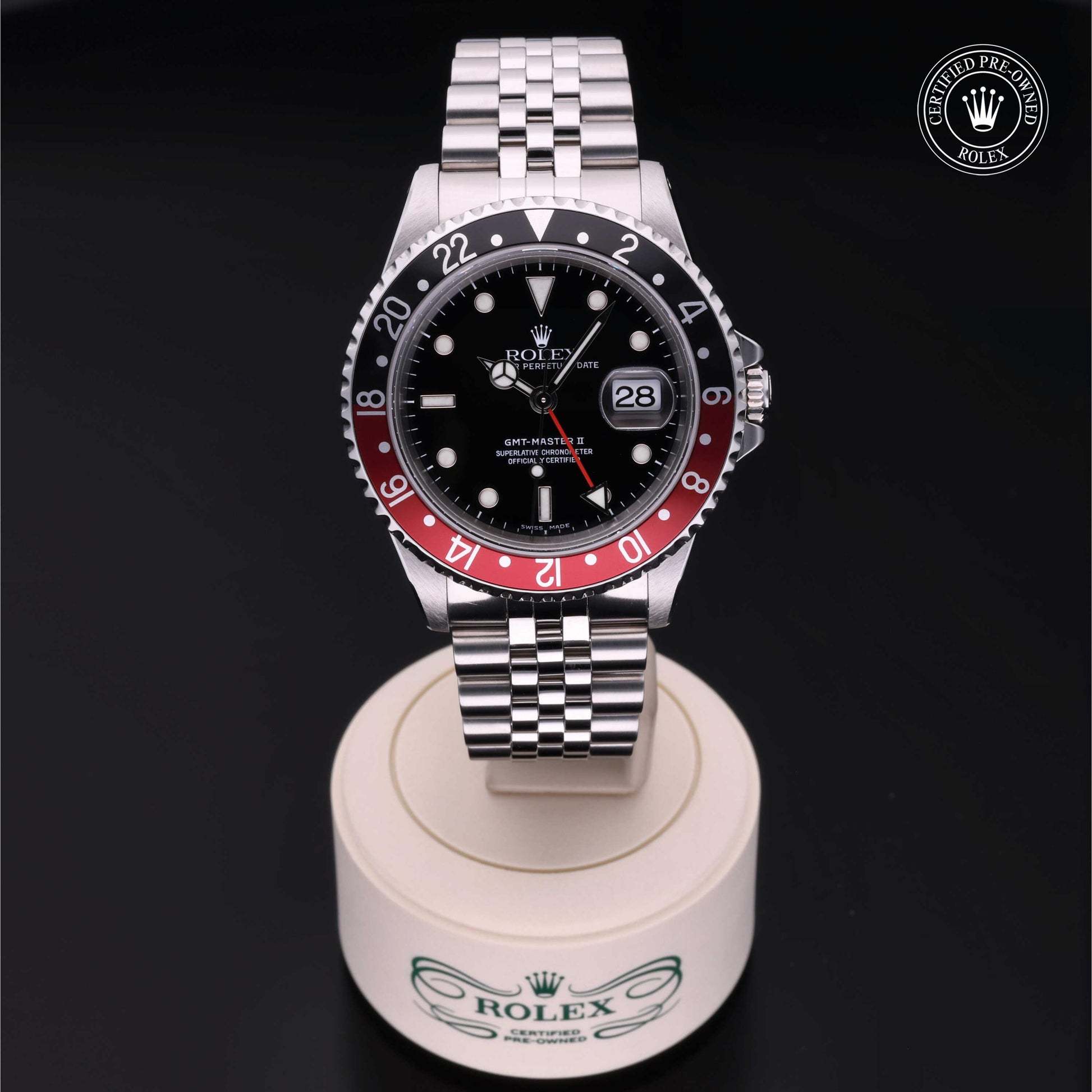 Rolex GMT-Master II with Jubilee bracelet, red and black bezel and black dial on a presentation stand against a black background.