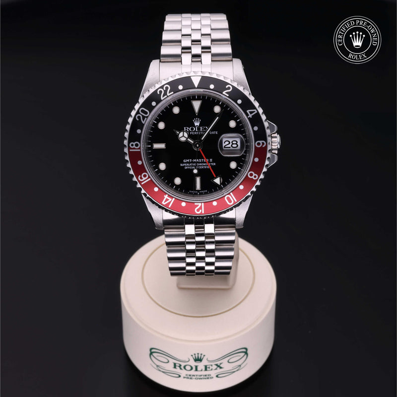 Rolex GMT-Master II with Jubilee bracelet, red and black bezel and black dial on a presentation stand against a black background.GMT-Master II