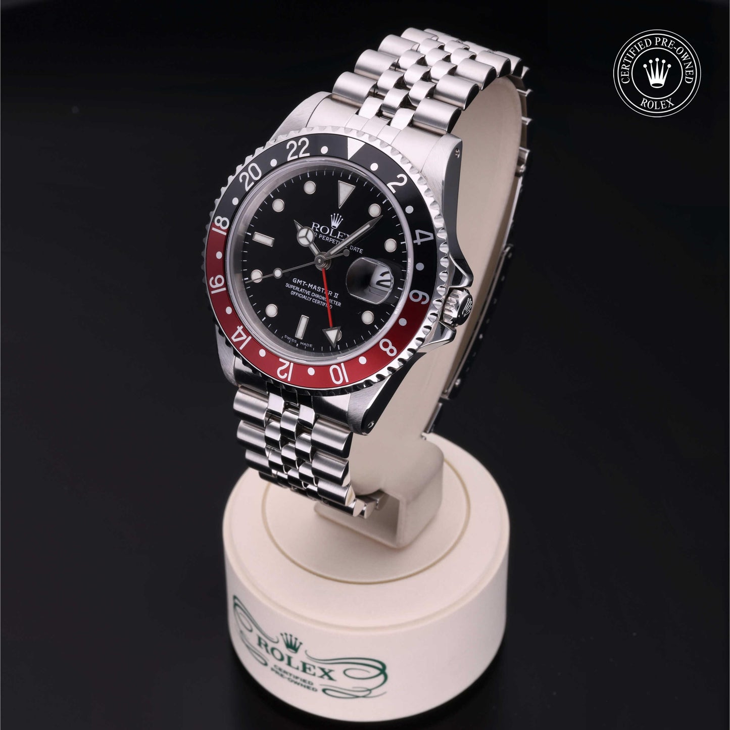 Rolex GMT-Master II with Jubilee bracelet, red and black bezel and black dial on a presentation stand against a black background.