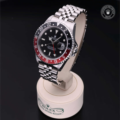 Rolex GMT-Master II with Jubilee bracelet, red and black bezel and black dial on a presentation stand against a black background.