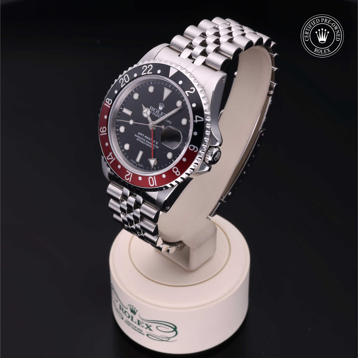 Rolex GMT-Master II with Jubilee bracelet, red and black bezel and black dial on a presentation stand against a black background.