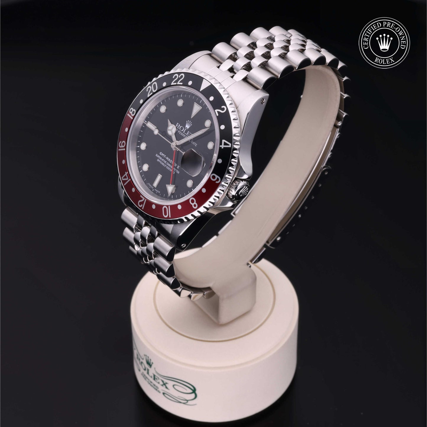 Rolex GMT-Master II with Jubilee bracelet, red and black bezel and black dial on a presentation stand against a black background.