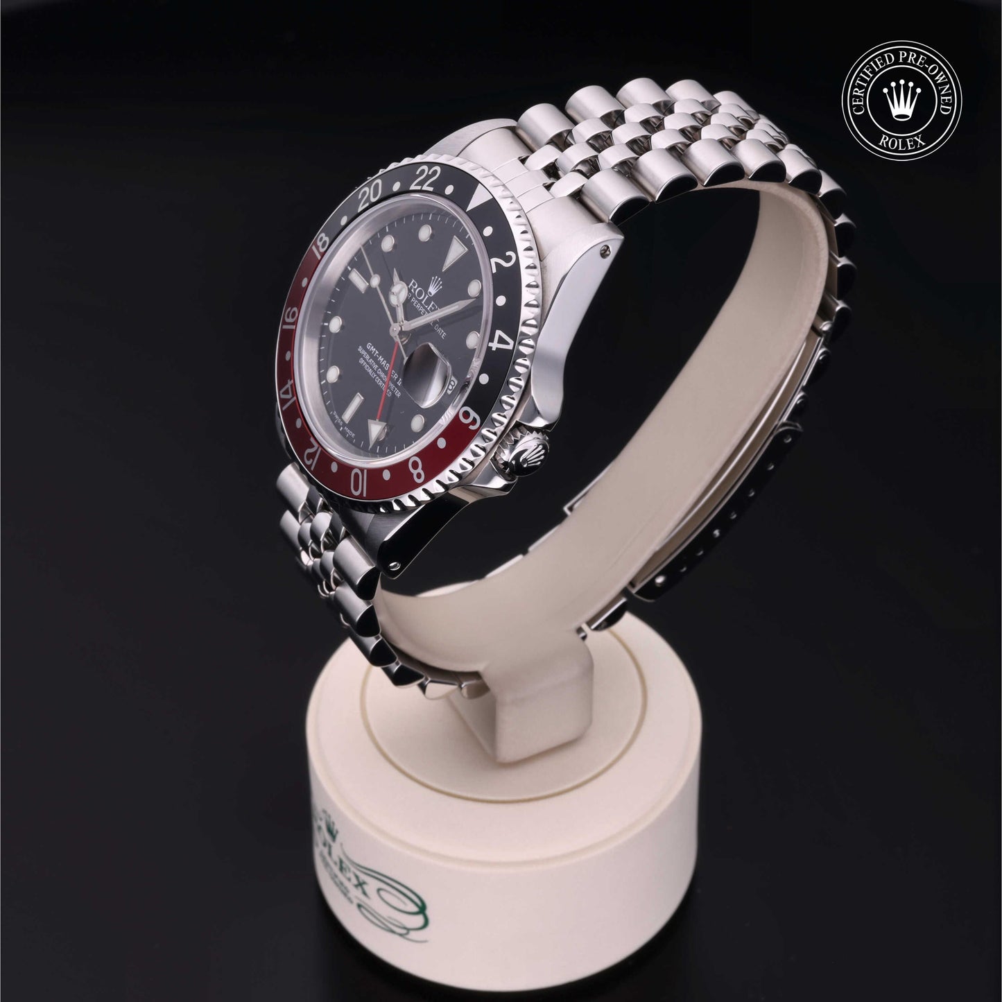Rolex GMT-Master II with Jubilee bracelet, red and black bezel and black dial on a presentation stand against a black background.