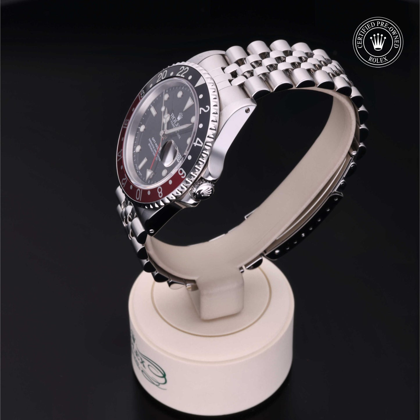 Rolex GMT-Master II with Jubilee bracelet, red and black bezel and black dial on a presentation stand against a black background.