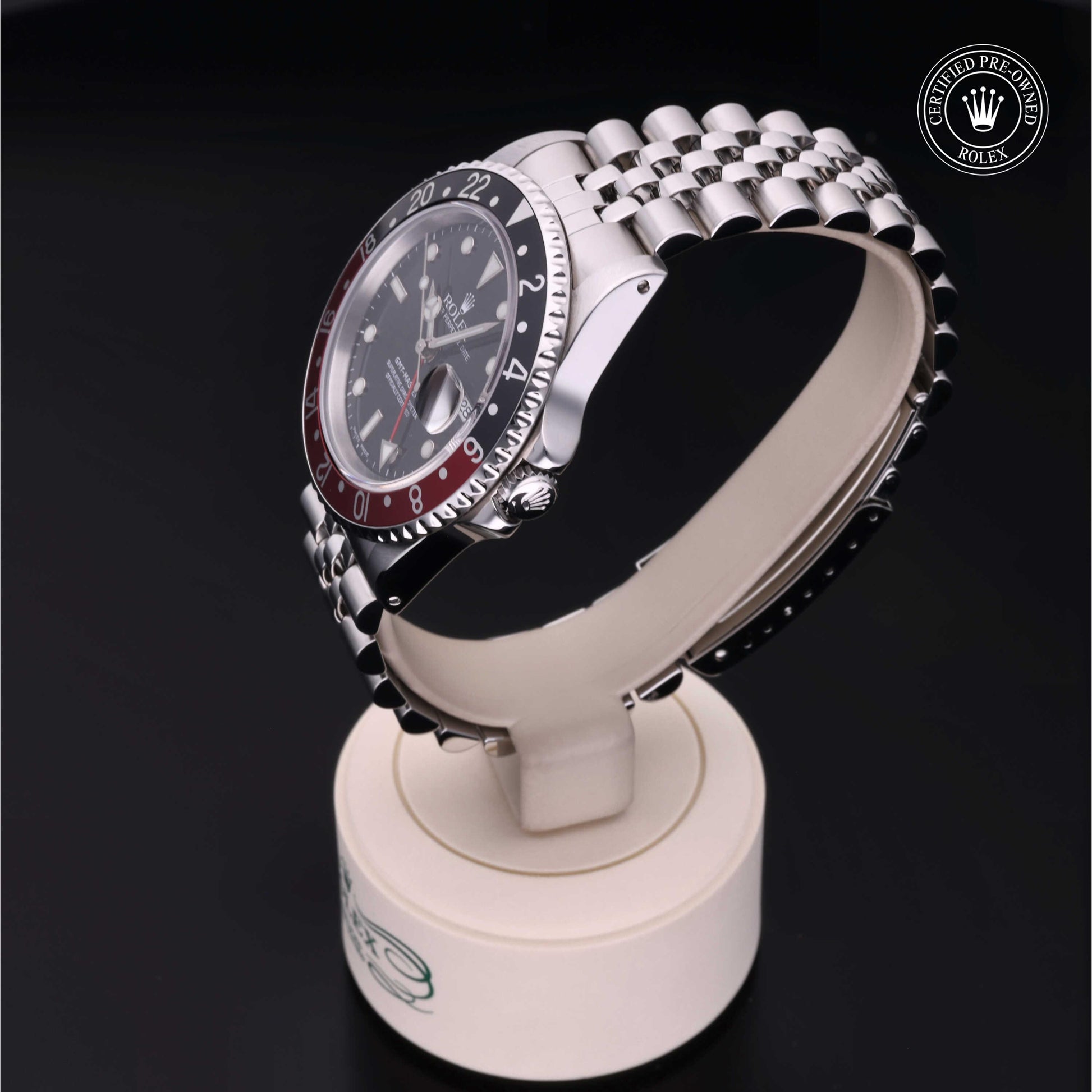 Rolex GMT-Master II with Jubilee bracelet, red and black bezel and black dial on a presentation stand against a black background.
