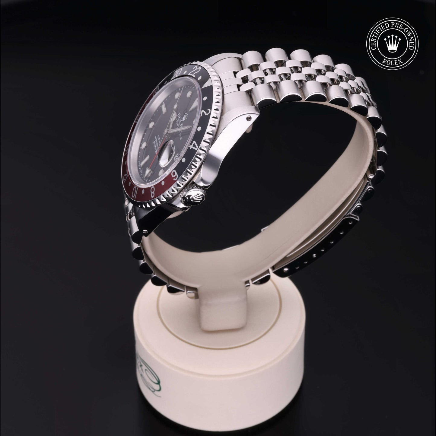 Rolex GMT-Master II with Jubilee bracelet, red and black bezel and black dial on a presentation stand against a black background.