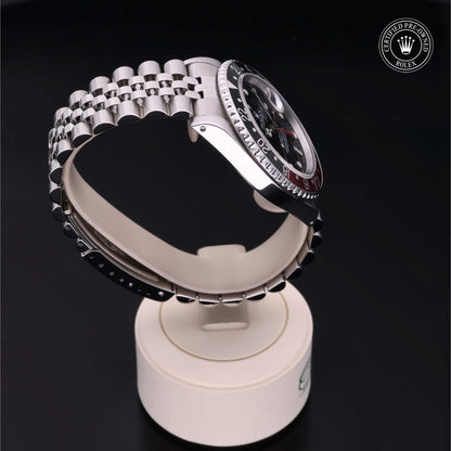 Rolex GMT-Master II with Jubilee bracelet, red and black bezel and black dial on a presentation stand against a black background.