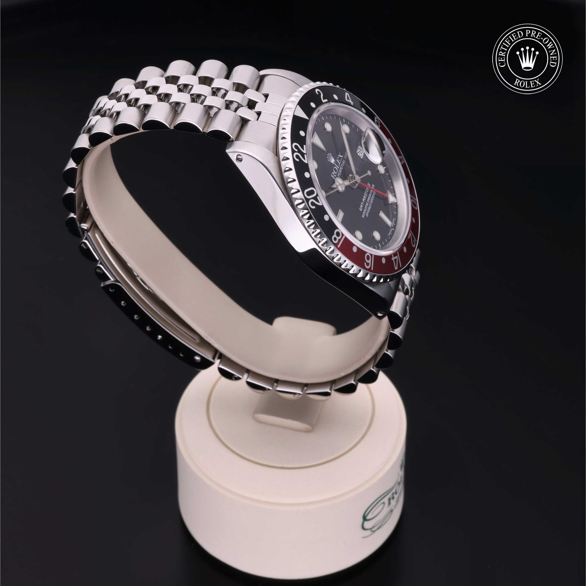 Rolex GMT-Master II with Jubilee bracelet, red and black bezel and black dial on a presentation stand against a black background.