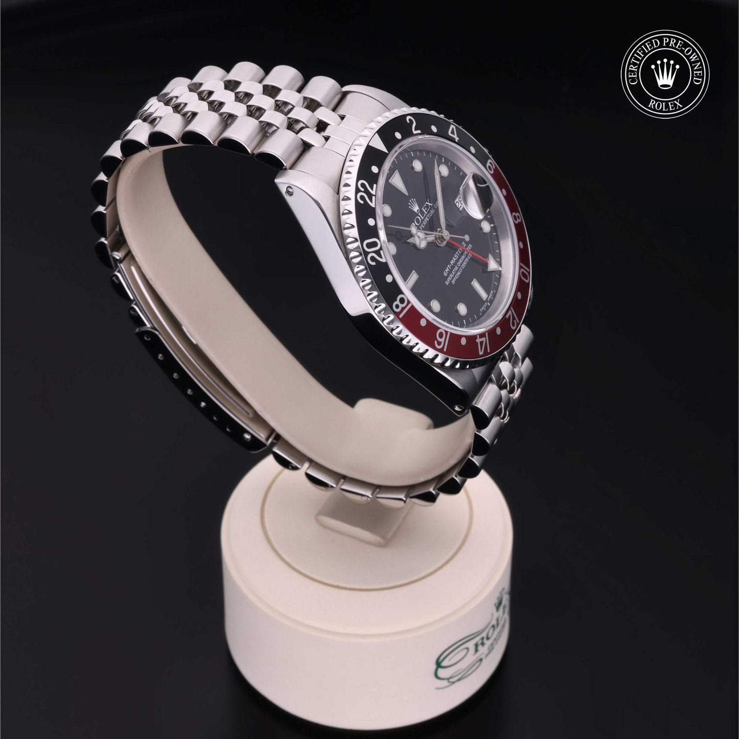 Rolex GMT-Master II with Jubilee bracelet, red and black bezel and black dial on a presentation stand against a black background.