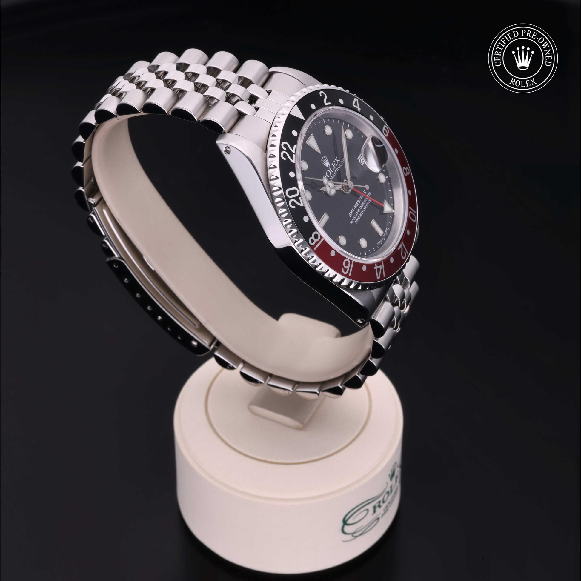 Rolex GMT-Master II with Jubilee bracelet, red and black bezel and black dial on a presentation stand against a black background.