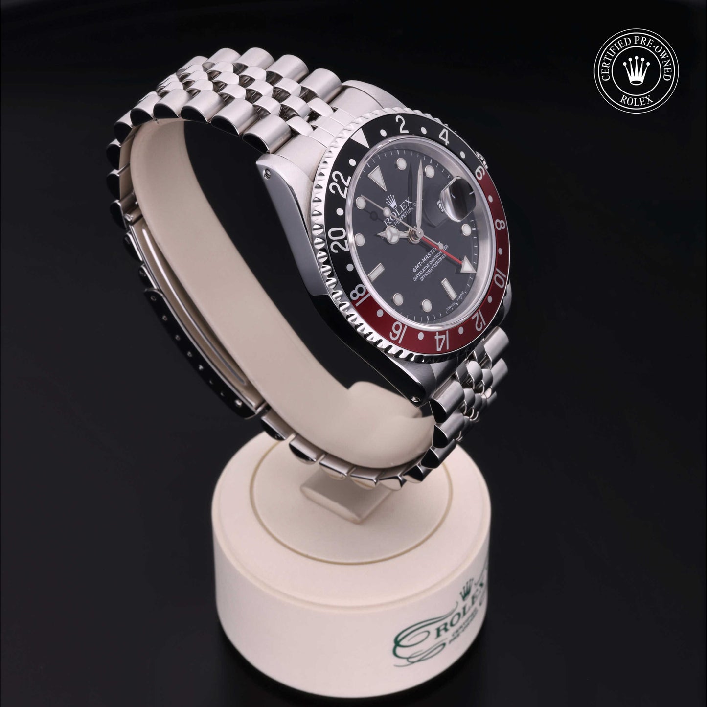 Rolex GMT-Master II with Jubilee bracelet, red and black bezel and black dial on a presentation stand against a black background.