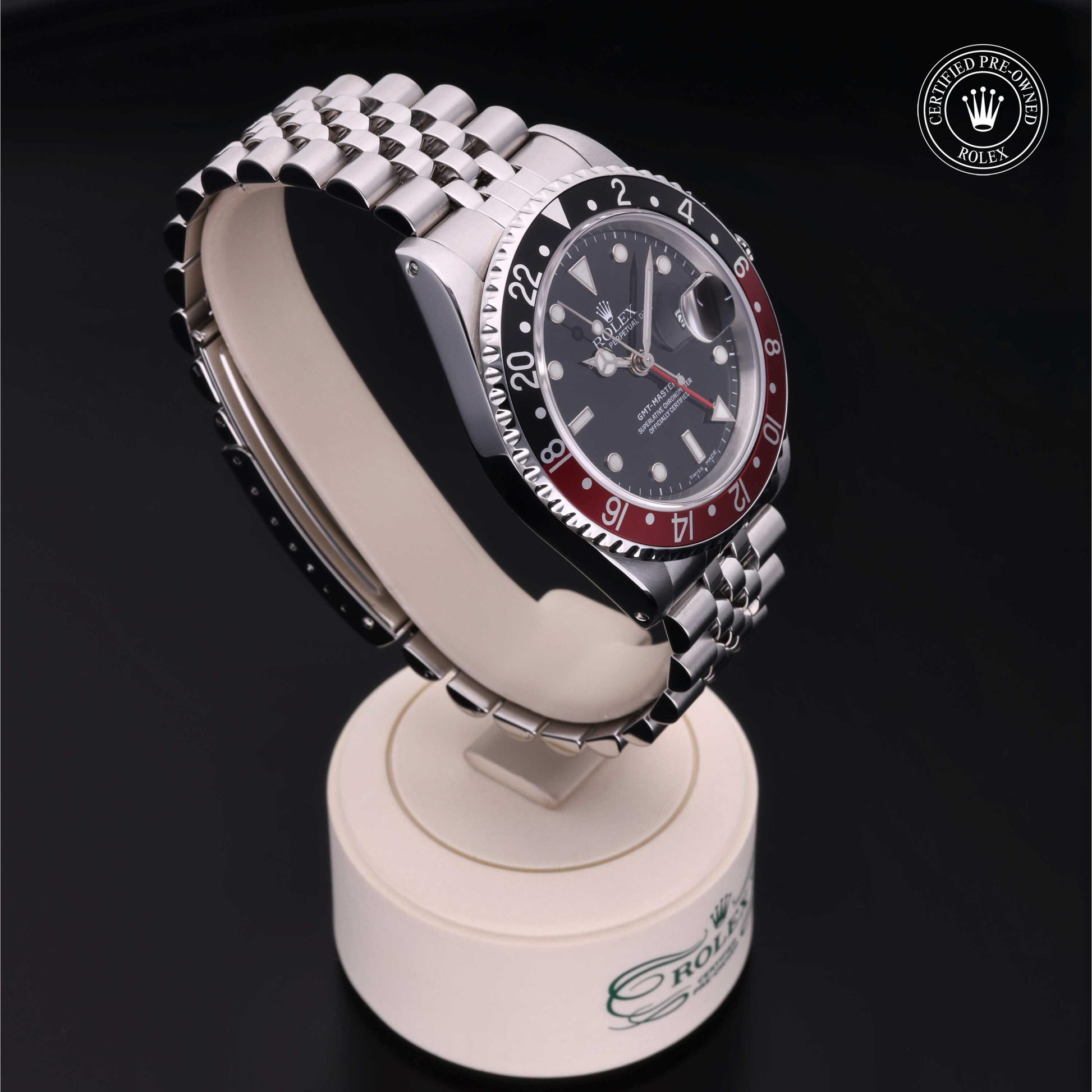 Rolex GMT-Master II with Jubilee bracelet, red and black bezel and black dial on a presentation stand against a black background.